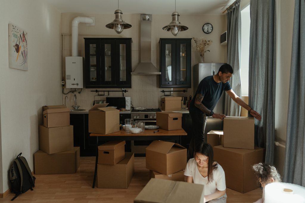 Man in Blue T-shirt Standing Near Brown Cardboard Boxes