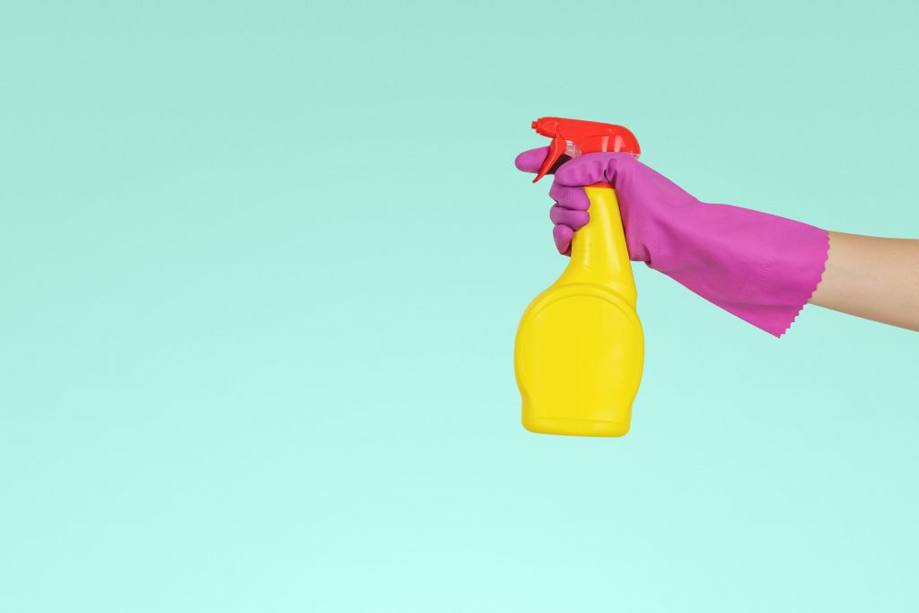 hand with spray bottle cleaning solution with pink glove