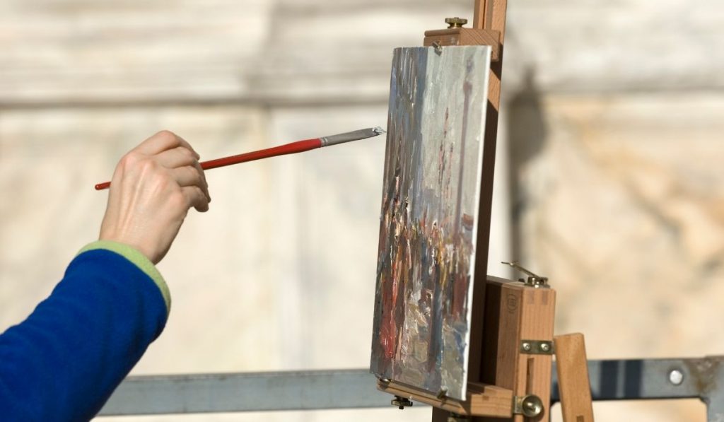 hand holding a paint brush and painting on a canva