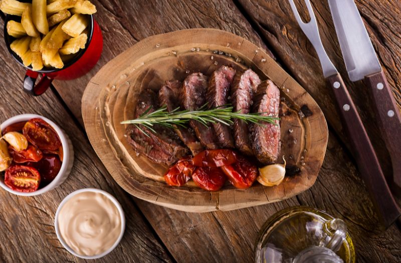 beautiful steak served on a wooden board with potatoe wedges, sun-dried tomatoes, mayo and olive oil on the side