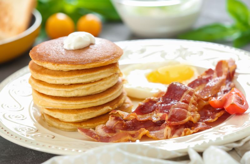 layers of pancakes with egg and bacon on the side