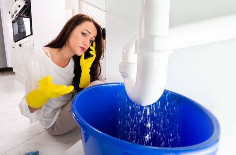 woman calling her landlord because there is a leak in the kitchen sink