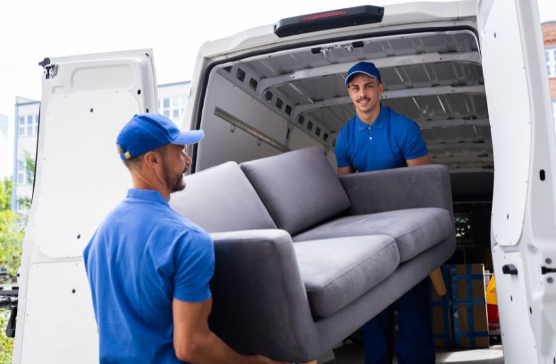 movers holding a two seater grey sofa