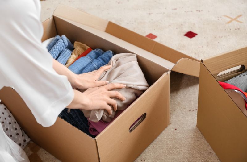 mommy packing old baby clothes in a cardboard box